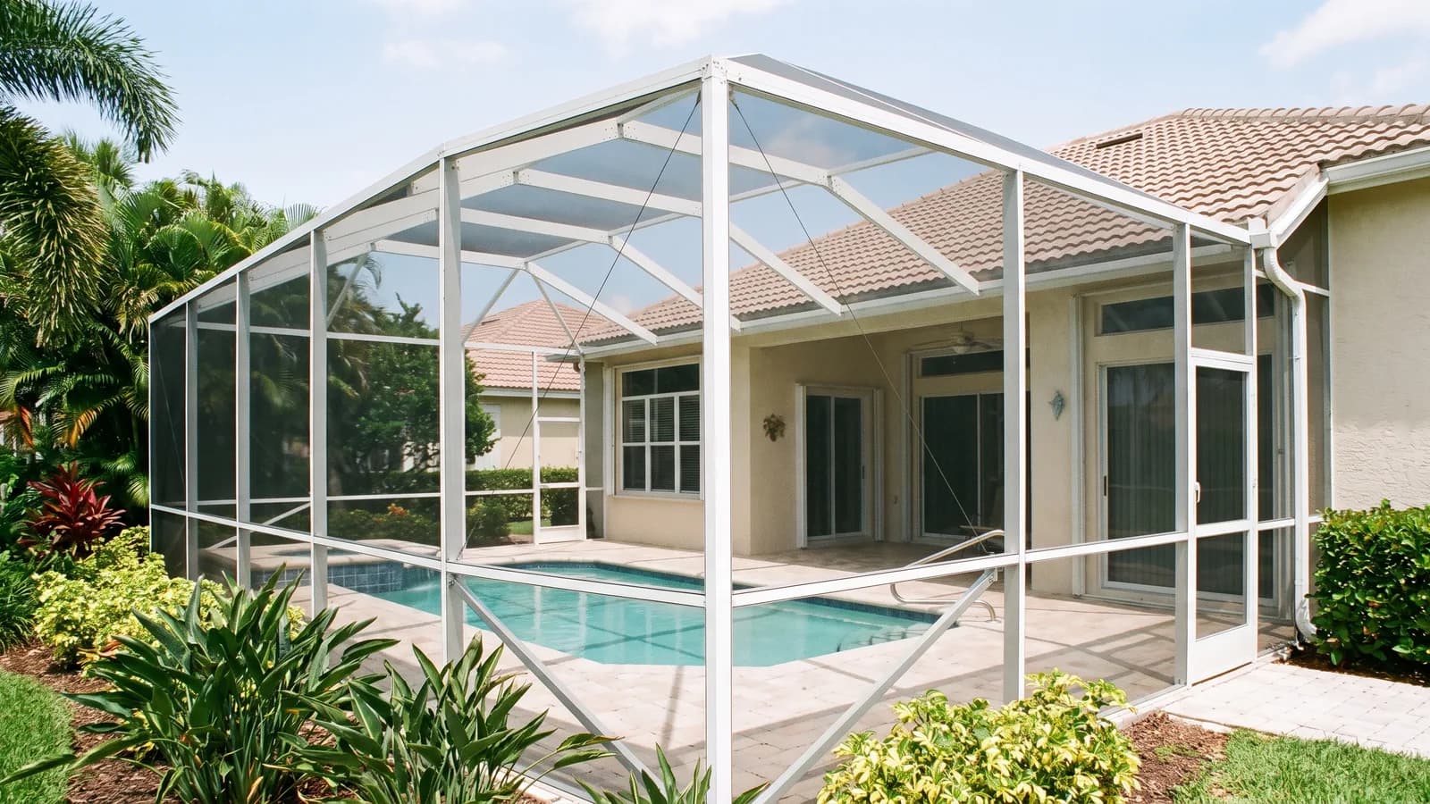 A screened pool enclosure (pool cage) attached to the back of a single-family Florida home under a bright sky.