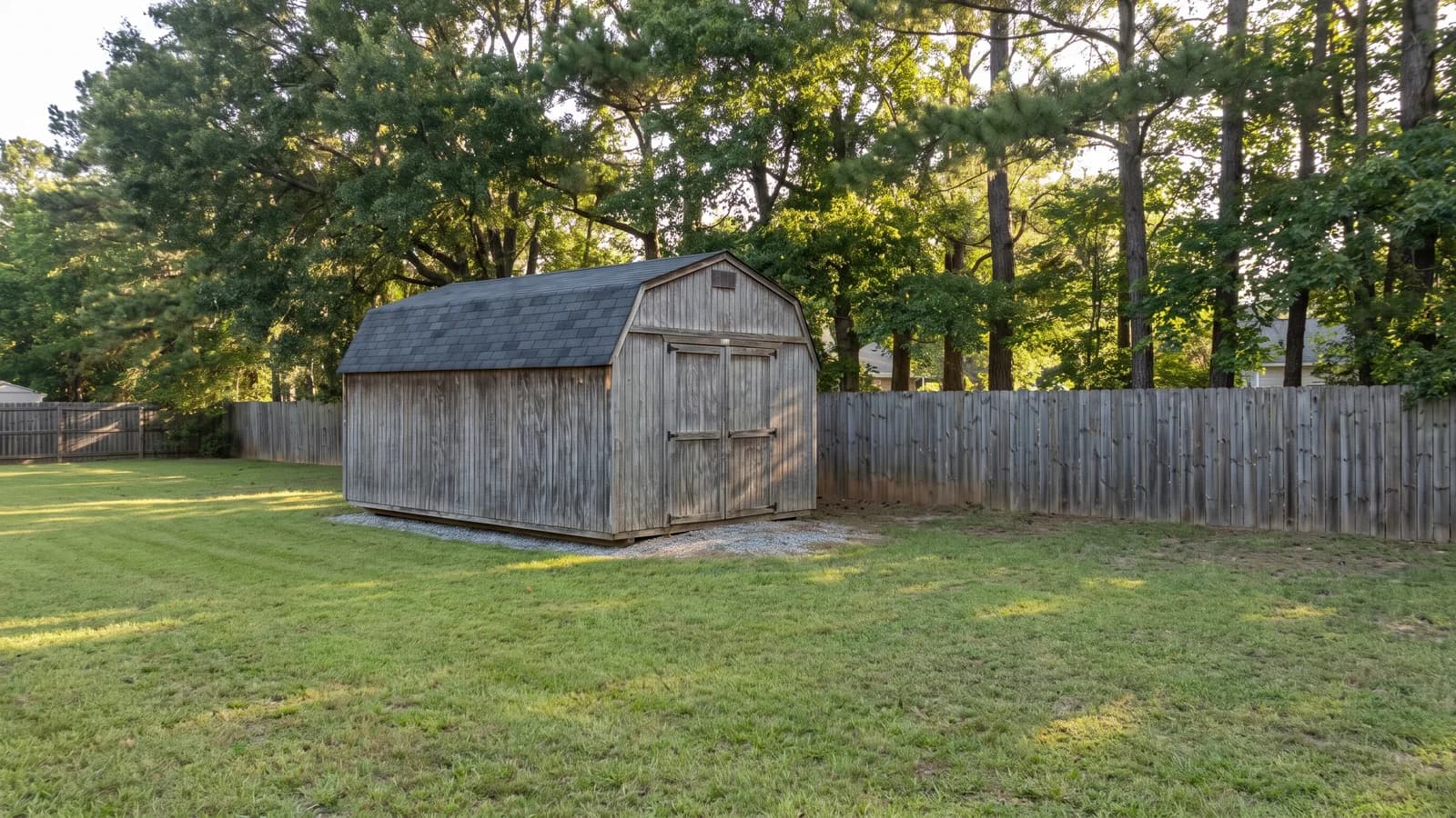 A detached wooden storage shed with a gable roof in the back yard of a suburban Georgia home
