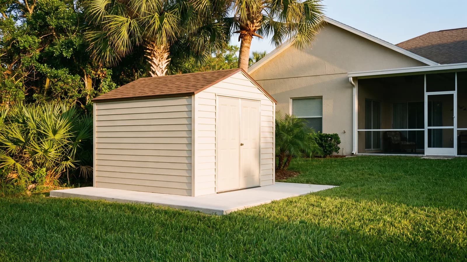 A small prefabricated backyard storage shed on a concrete pad behind a single-family Florida home in warm afternoon light.