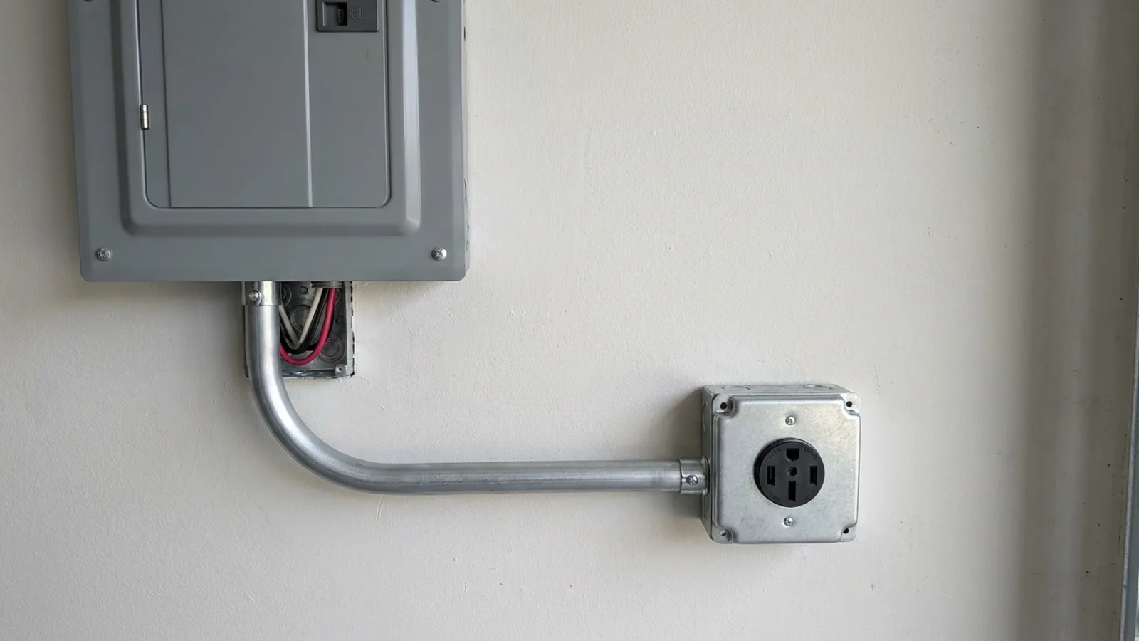 A close view of a dedicated 240-volt circuit and conduit running from an electrical panel to a garage wall